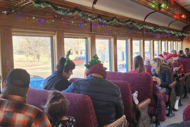 People in festive hats on a decorated train with colorful lights and garlands.