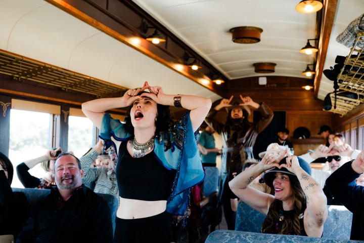 People on a train making triangle shapes with their hands over their heads.