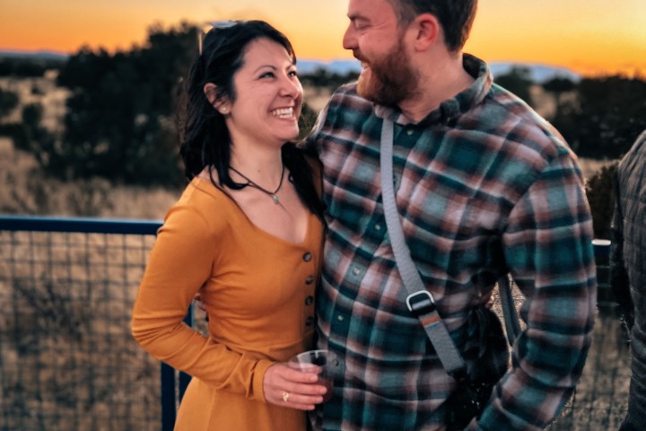 Couple smiling at each other on a deck during sunset.