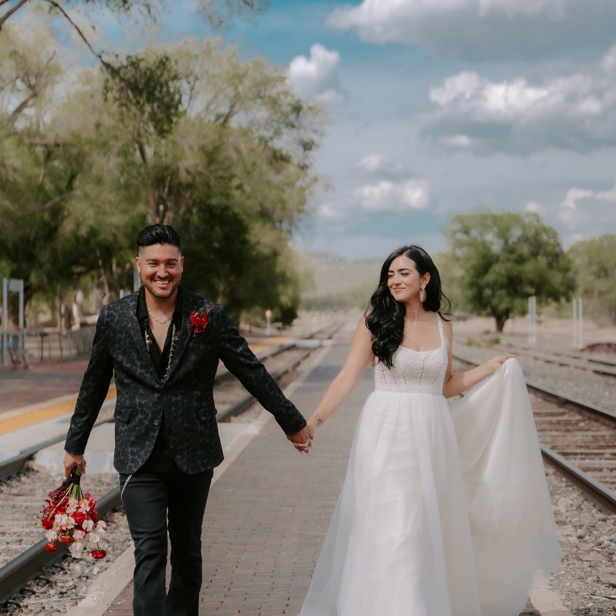 Couple in wedding attire holding hands on a railway platform.