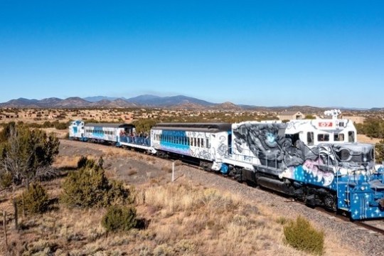 Colorful train with graffiti art traveling through a desert landscape.