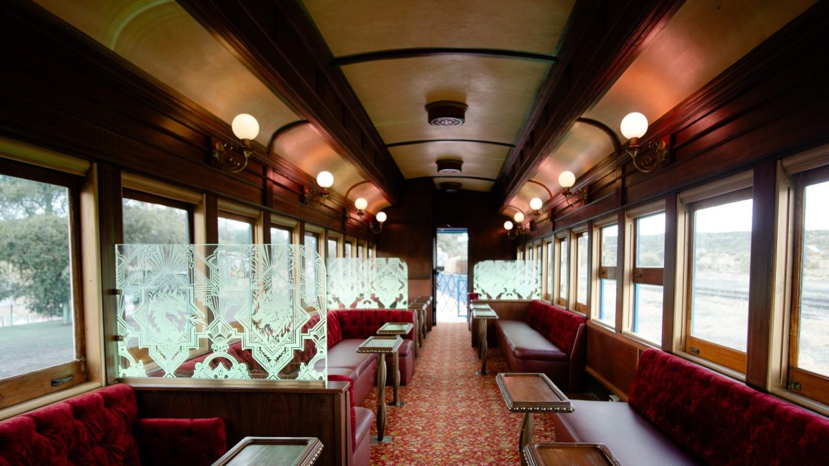 Vintage train interior with red velvet seats and wooden tables.